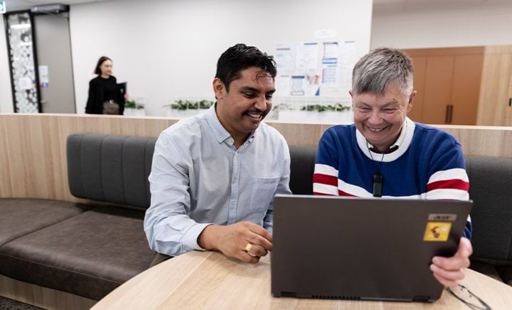 Two men sitting at a round table working on a laptop.