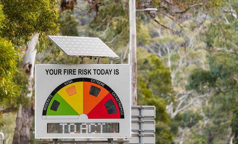 A fire safety sign with a solar panel mounted on top in the bush.