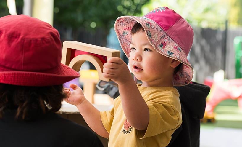 A child stands in front of an educator, playing with a wooden toy.