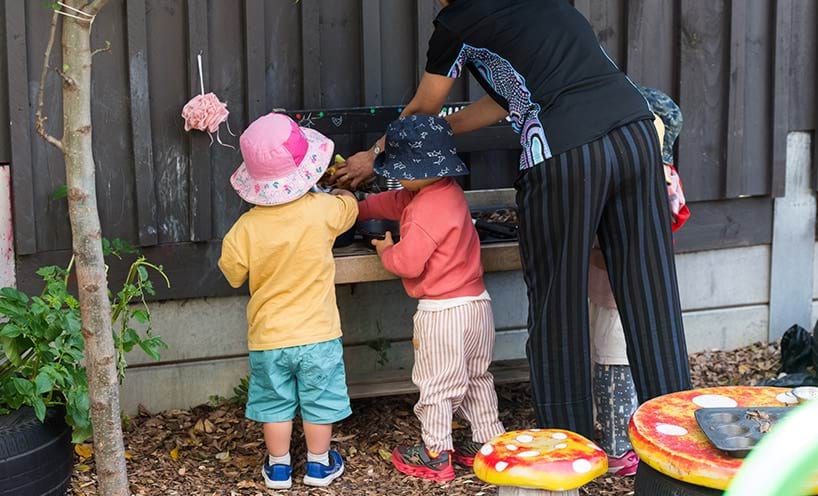Three young children and an educator playing outdoors.