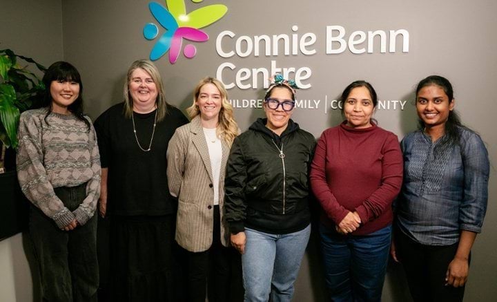 A group of 6 women standing in front of a wall with the words 