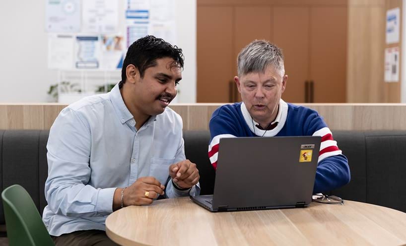 Two men sitting at a round table working on a laptop.