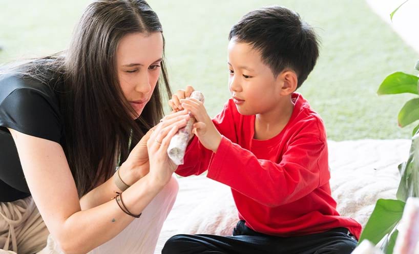 A woman and a young boy sit on the floor together, examining a rolled object.