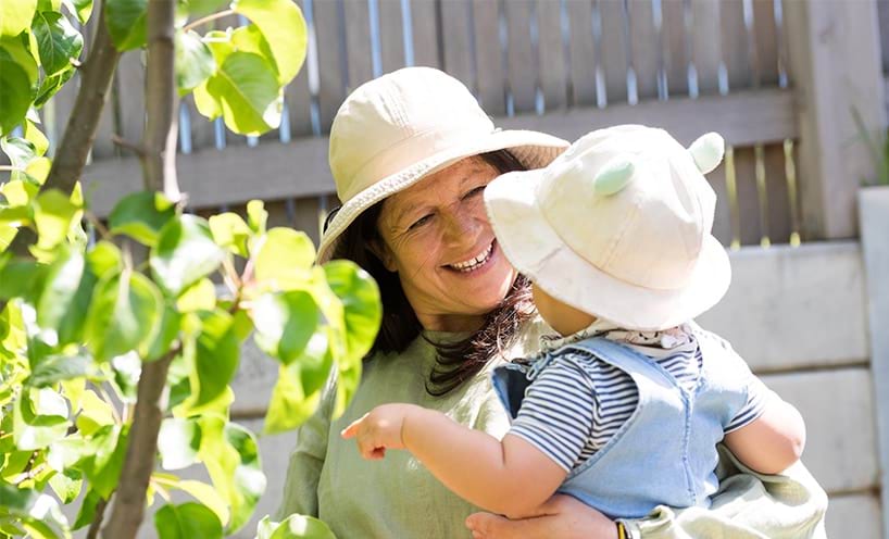 Female educator holding an infant outside in garden.