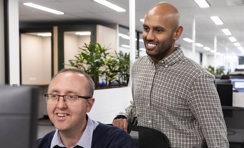 Two staff members at a desk in an open plan office.