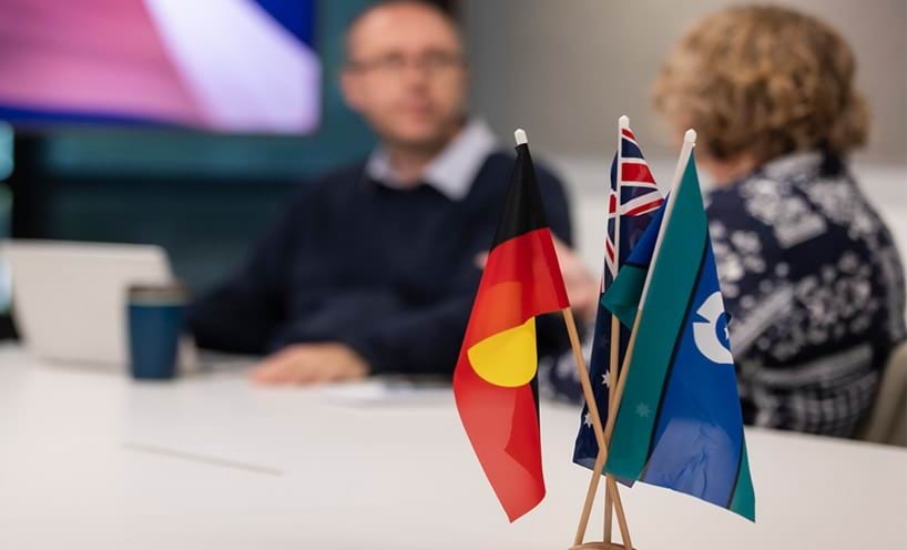 Three flags at a work desk with the First Nations flag in red, yellow and black.