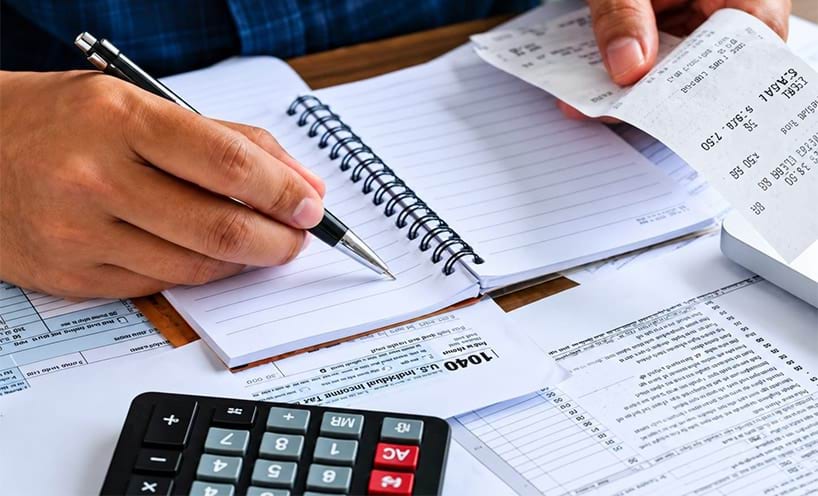 hand holding a pen checking a notepad with a calculator and a receipt